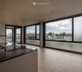 Modern kitchen with dark countertops, light wooden flooring, and large windows offering a view of the cityscape.