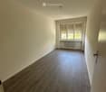 Empty hallway with wooden flooring, white walls, and a window with blinds on the right side.