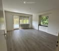 Empty room with wooden flooring, white walls, large windows, and a radiator. No furniture or equipment present.