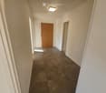 Empty hallway with tiled floor, white walls, and two doors (one wooden, one white).