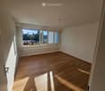 Empty room with wooden flooring, large windows, and white walls. No furniture or equipment present.
