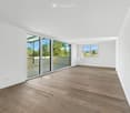 Empty room with white walls, wooden flooring, large sliding glass doors leading to a balcony, and a window with a scenic view.