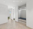 Empty room with white walls, tiled floor, built-in closet with drawers and a bench, and a doorway leading to another space.