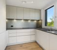 Modern kitchen with white cabinets, stainless steel sink, and a sleek faucet. The space features a large window with a view of greenery outside.