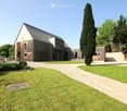 Modern two-story house with wooden exterior, large windows, and a spacious lawn with a gravel driveway.
