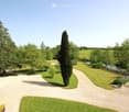 A well-maintained garden with a gravel driveway, tall trees, a pond, and neatly trimmed grass.