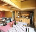 A cozy, well-furnished living and dining area with exposed wooden beams, a sofa, dining table, chairs, and a kitchen area with cabinets and appliances.