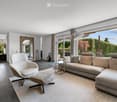 Modern living room with large windows offering a view of the garden, featuring a sectional sofa, armchair, ottoman, coffee table, and a floor lamp.