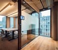 Modern office space with large glass windows, a wooden table, and chairs, featuring a sleek design and natural light.