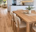 Open-plan kitchen and dining area with light wood flooring, white cabinets, a central dining table with four chairs, a sofa, coffee table, and a modern oven.