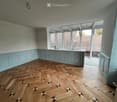 Empty room with light blue walls, wooden herringbone floor, and large windows overlooking a tiled roof.