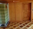 Empty room with wooden walls, wooden floor, and a green tiled stove. No furniture or equipment present.