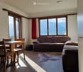 Bright living room with large windows offering a mountain view, featuring a sofa, ottoman, dining table, chairs, and a fur rug.