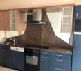 Modern kitchen with dark blue cabinets, stainless steel appliances, and a textured backsplash. Features include a sink, faucet, oven, dishwasher, refrigerator, and range hood.