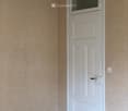 Empty room with wooden flooring, beige walls, and a white door with a window at the top.