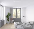 Modern, minimalist bedroom with a large window, grey bedding, a wooden chair, a small table, a floor lamp, and a leafy plant in a pot.