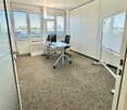 Office space with a desk, chair, computer, and whiteboard, large windows with blinds, and carpeted floor.
