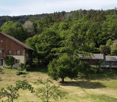 A scenic view of a rural property with multiple wooden houses surrounded by lush green trees and rolling hills.