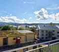 View of a residential complex with modern buildings, green roofs, and surrounding greenery under a clear blue sky.