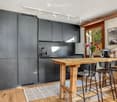 modern kitchen with wooden countertop, black cabinets, tiled floor, flowers on the counter, 3 bar stools