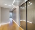Modern hallway with wooden flooring, recessed lighting, glass partitions, and a patterned wall design.