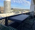 Balcony with a table and chairs, overlooking a cityscape with modern buildings and a clear blue sky.