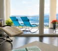 Balcony with a scenic view, featuring two blue lounge chairs, a white lounge chair, a small table, and flower pots.