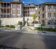 Modern multi-story residential building with balconies, concrete steps, and greenery around the entrance.