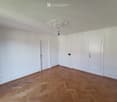Empty room with white walls, wooden herringbone flooring, and a decorative ceiling light fixture.