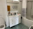 Modern bathroom with white tiles, a white sink cabinet, a large mirror, a toilet, and a bathtub with a shower curtain.