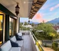 Balcony with wicker chairs, small table, and scenic mountain view.