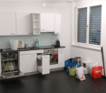 Modern kitchen with white cabinets, black countertops, and stainless steel appliances. Features a dishwasher, oven, sink, and various items including a backpack and handbags.