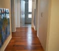 A long, well-lit hallway with wooden flooring, white walls, and a door at the end leading to another room.