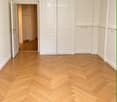 Empty hallway with herringbone-patterned wooden flooring, white walls, and double doors.