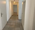 Empty hallway with tiled floor, white walls, and several doors leading to other rooms. Minimal lighting from ceiling fixtures.