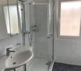 Modern bathroom with a white sink, chrome faucet, large mirror, and a glass-enclosed shower stall.