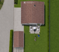 Aerial view of a house with a well-maintained lawn, patio area with outdoor furniture, and a small greenhouse attached to the side.