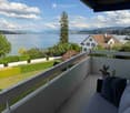 Balcony with a sofa, potted cactus, and scenic view of a lake and mountains.