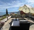 Balcony with a view of the lake and mountains, featuring a sofa, table, and umbrella.