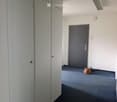 Empty hallway with grey cabinets on one side, a closed door at the end, and a small brown bag on the floor.