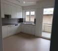 Modern kitchen with white cabinets, stainless steel appliances, and a large window overlooking a brick wall.