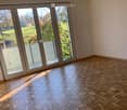 Empty room with wooden herringbone flooring, large sliding glass doors leading to a balcony, and natural light streaming in.