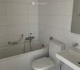 A small bathroom with white tiled walls and black tiled floor, featuring a toilet, bathtub, and sink.