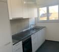 Modern kitchen with white cabinets, black countertops, a sink, and an oven. The space is well-lit with a window offering a view of the outside.