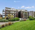 Modern multi-story residential building with balconies, surrounded by well-maintained green lawn and shrubs.