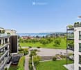 Modern multi-story residential building with balconies, surrounded by green lawns, trees, and a scenic lake view in the background.