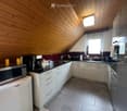 Modern kitchen with white cabinets, stainless steel appliances, and wooden ceiling beams. Features include a microwave, coffee maker, sink, and various kitchen items on the counter.
