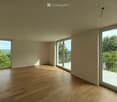 Empty room with wooden flooring, large windows, and sliding glass doors leading to a balcony.
