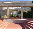 A covered outdoor area with a brick floor, potted plants, and steps leading to a building entrance.
