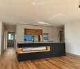 Modern kitchen with light-colored cabinets, dark lower cabinets, a central island, and a sleek sink with a modern faucet. The space features wooden flooring and recessed lighting.